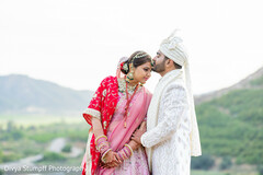 Bride in Pink Lehenga and Groom in White Sherwani with Mountainous Backdrop