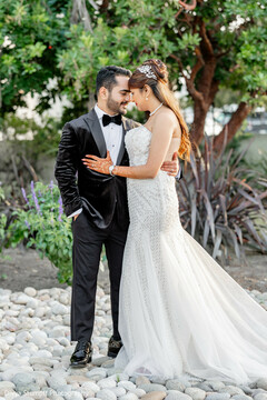 Couple in Black Tuxedo and White Gown Amidst Greenery and Pebbles
