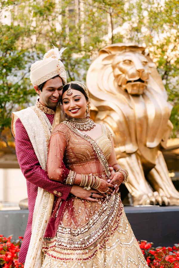 wedding portrait,gold lehenga,maroon sherwani,bridal jewelry,groom fashion,wedding attire,couple pose,golden lion statue