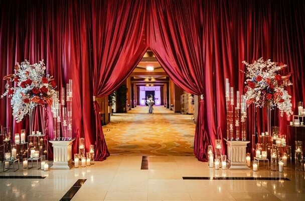 wedding entrance,red drapes,floral decor,candlelit aisle,luxury wedding,event design,grand entrance,south asian wedding decor,elegant lighting,reception decor