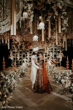 Couple Poses on Lavish Stage with Hanging Decor and Floral Arrangements