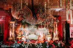 Elaborate Stage Decor with Hanging Gold Accents and Floral Arrangements