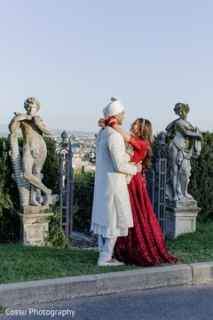 Couple Embracing in Red Lehenga and White Sherwani with Sculptural Backdrop