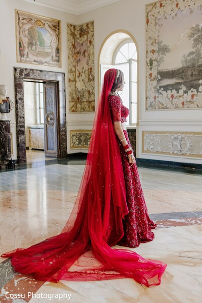 red lehenga,bridal fashion,flowing veil,south asian wedding,bridal portrait,grand venue,opulent setting,elegant bride,traditional attire,red bridal outfit
