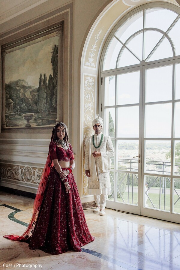 bridal portrait,deep red lehenga,ivory sherwani,groom fashion,bridal fashion,wedding attire,elegant hall,arched windows